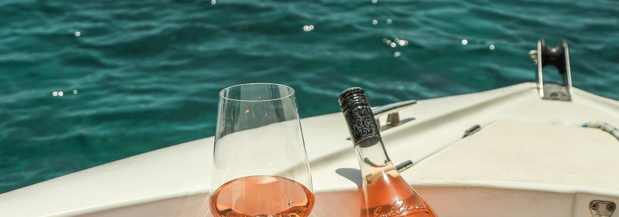 Glas Rose und Flasche auf einem Boot, Mittelmeer im Hintergrund