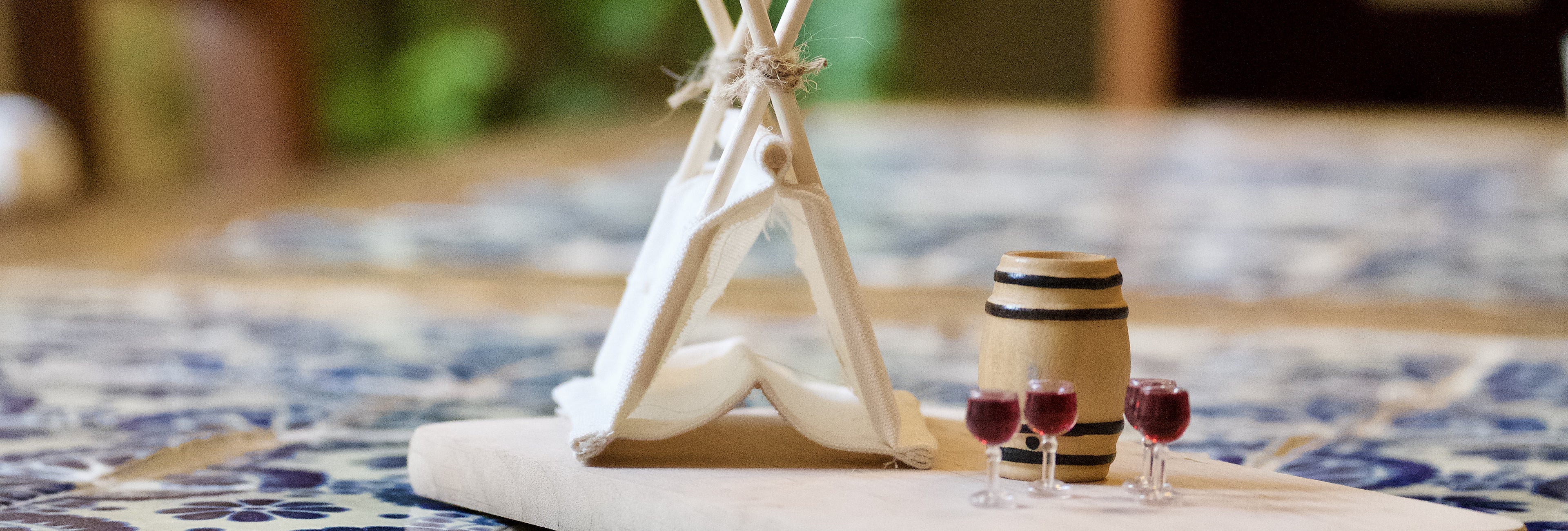 Miniatur-Weinzelt mit Weinfass und zwei Glaeschen Rotwein auf einer Holzplatte