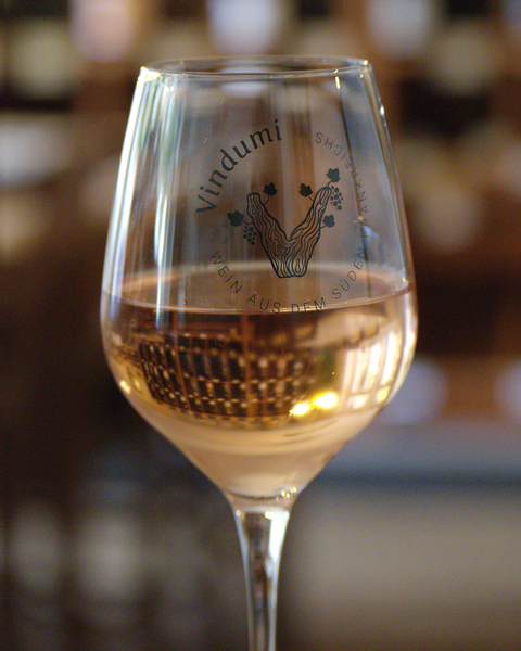 Glas Rosé vor dem Weinregal bei Vindumi